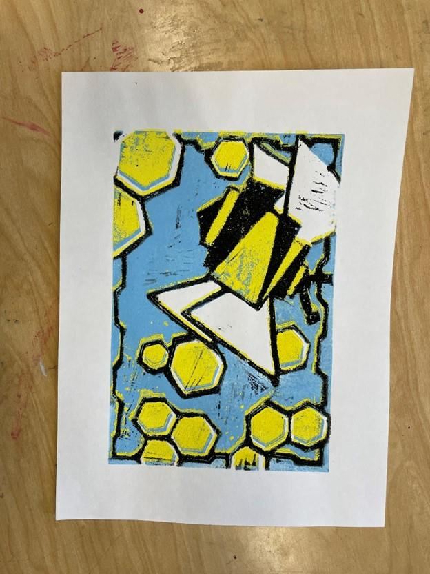 Color print on a white canvas sitting on a table. The print shows an abstract bumblebee and honeycomb with a blue background